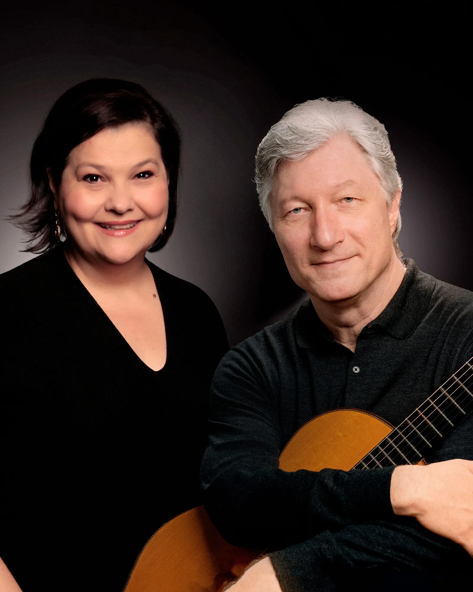 Retrato de uma cantora de cabelo curto e de um violonista grisalho com violão, sobre fundo escuro