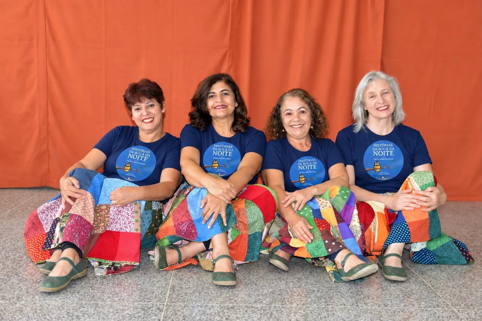 Quatro integrantes do Grupo Paepalanthus sentadas, com camisetas do projeto e saias de retalhos